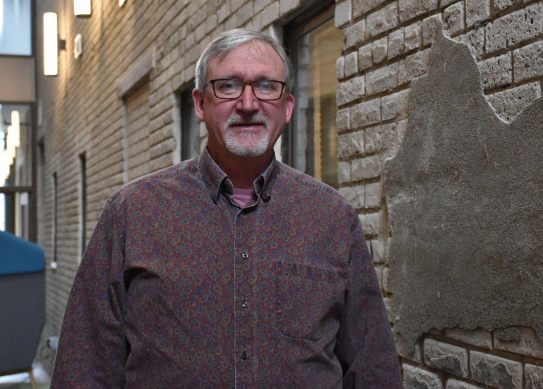 Man in dark red button up shirt standing at a brick wall